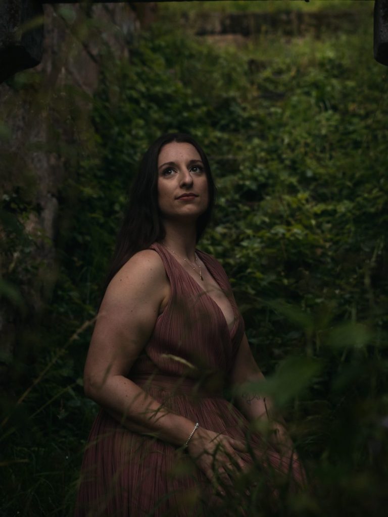 Frau in schwarzem Kleid steht zwischen blühenden Kirschbäumen und lächelt.