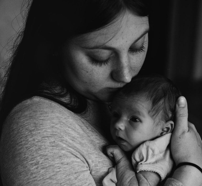 Eine Mutter hält ihr Neugeborenes liebevoll im Arm und legt den Kopf darauf.
