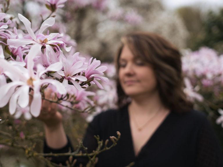 Frau streichelt zarte, rosa Magnolienblüten in einer blühenden Landschaft.