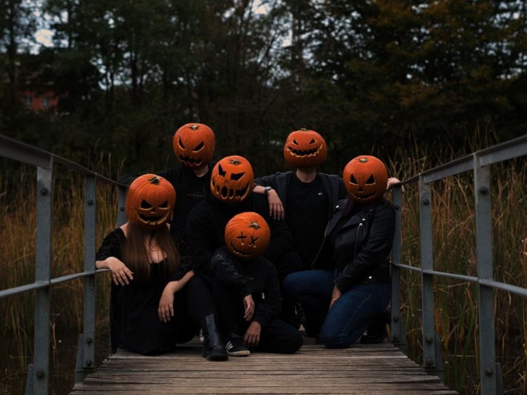 Sechs Personen mit Kürbiskopfmasken posieren auf einer Holzbrücke im Freien.