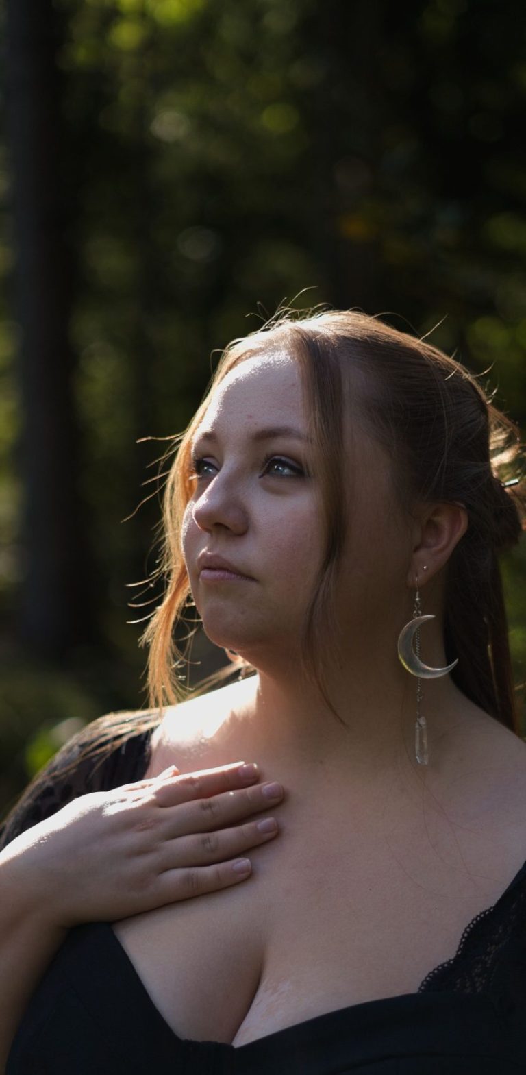 Frau mit langen Haaren in einem schwarzen Oberteil, nachdenklicher Blick in der Natur.