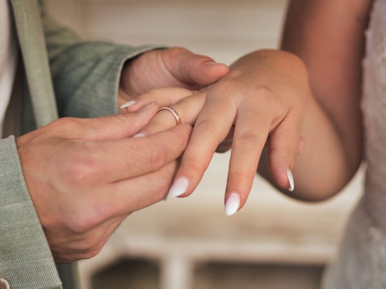 Hände, die einen Ring beim Hochzeitstradition an einen Finger anstecken.