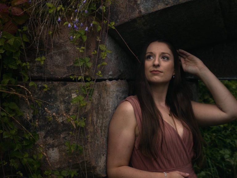 Frau in schwarzer Kleidung geht durch einen engen, säulenartigen Gang.